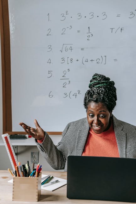 Positive smart African American female tutoring online with netbook in classroom with whiteboard